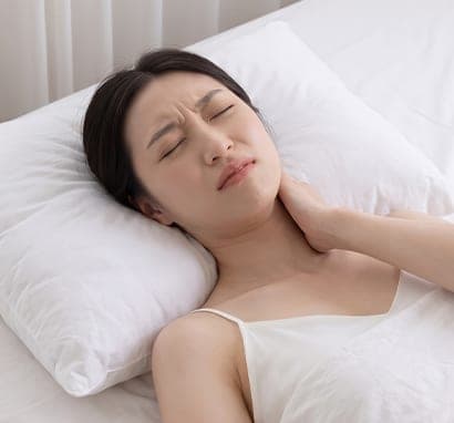일반 베개를 베고 누워 한 손으로 목을 잡고 얼굴을 찡그린 여성